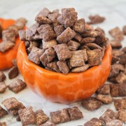 Pumpkin Spice Muddy Buddies in a pumpkin jar with some spilled on the table around it