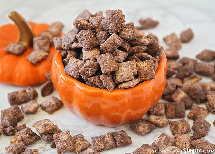 Pumpkin Spice Muddy Buddies in a pumpkin jar with some spilled on the table around it