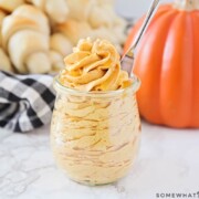 piped Whipped Pumpkin Honey Butter inside a glass jar in front of a basket of dinner rolls