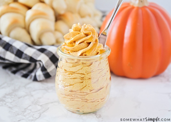 piped Whipped Pumpkin Honey Butter inside a glass jar in front of a basket of dinner rolls