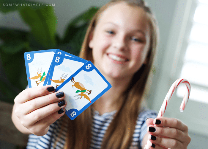 a young girl holding a candy cane instead of a spoon and four cards that match showing she won the game of spoons