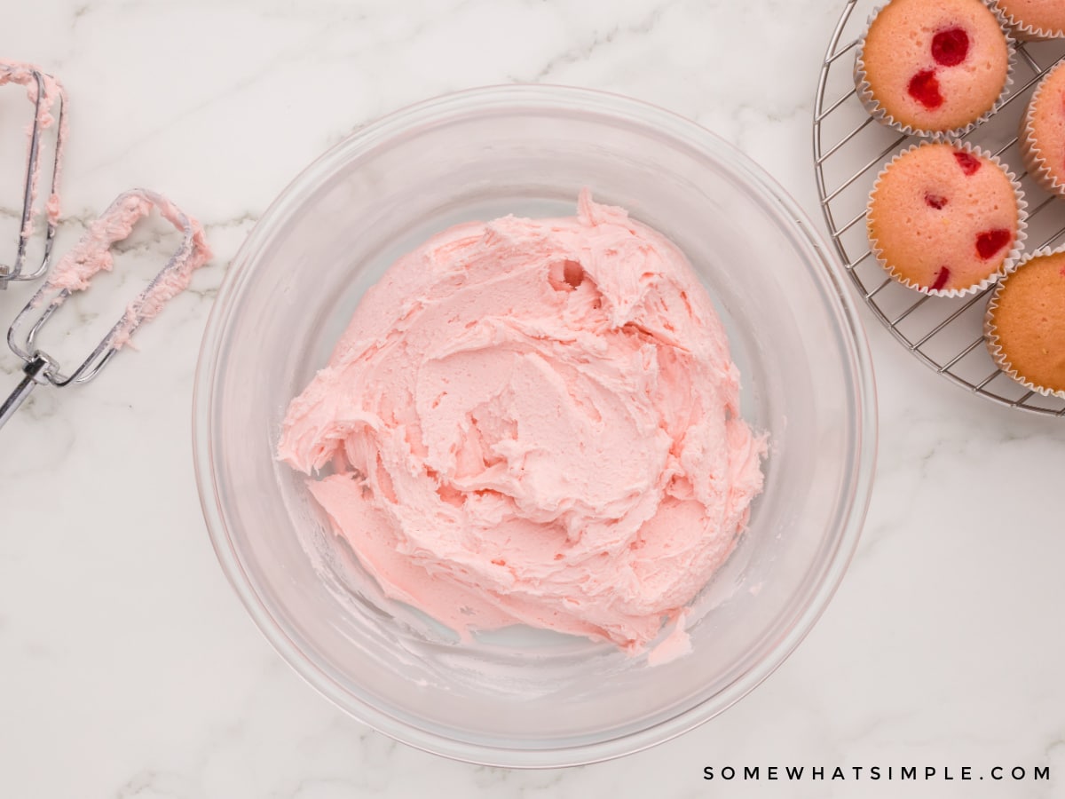 making cherry buttercream frosting in a glass bowl