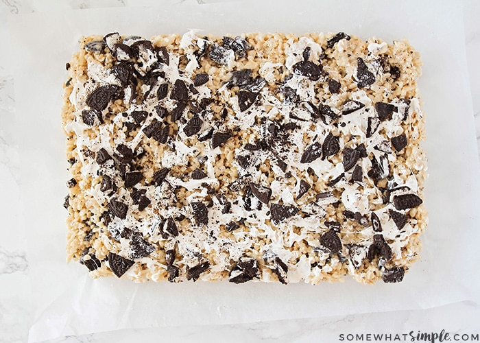 looking down on a rectangle of rice krispie treats just taken out of the pan. These treats are topped with Oreo cookies with white chocolate drizzled over the top.