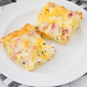 two squares of a croissant breakfast egg casserole made with ham on a white plate sitting on top of a cloth black and white striped napkin.