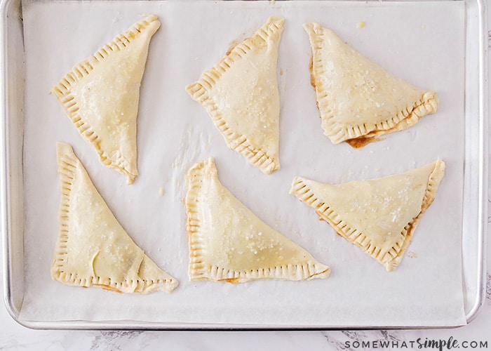 six raw apple turnovers made with puff pastry on a baking sheet lined with parchment paper ready to go in the oven
