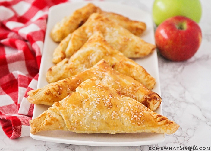 a long white serving tray with six golden brown apple turnovers on it in a line