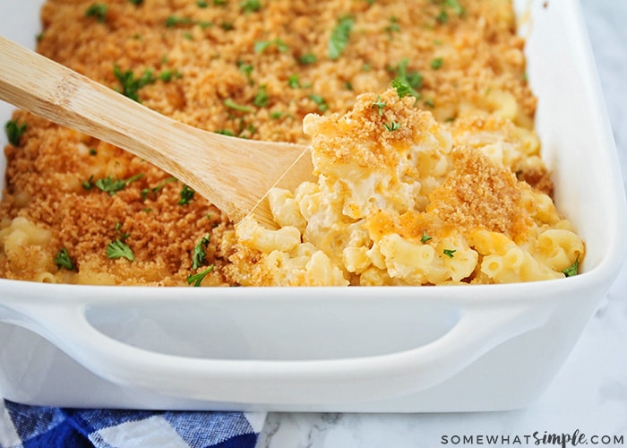 a casserole pan filled with homemade macaroni and cheese that was baked in the oven. A wooden spoon is beginning to lift our a scoop of food.