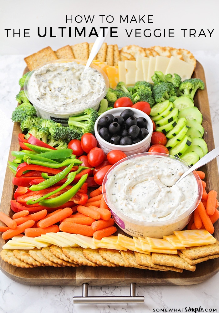 a colorful veggie tray idea that's filled with crackers, cheese, broccoli pieces, cucumber slices, cherry tomatoes, olives, red and green bell pepper slices, baby carrots and two vegetable dips all on a dark acacia wood serving tray with the words how to make the ultimate veggie tray written at the top of the image.