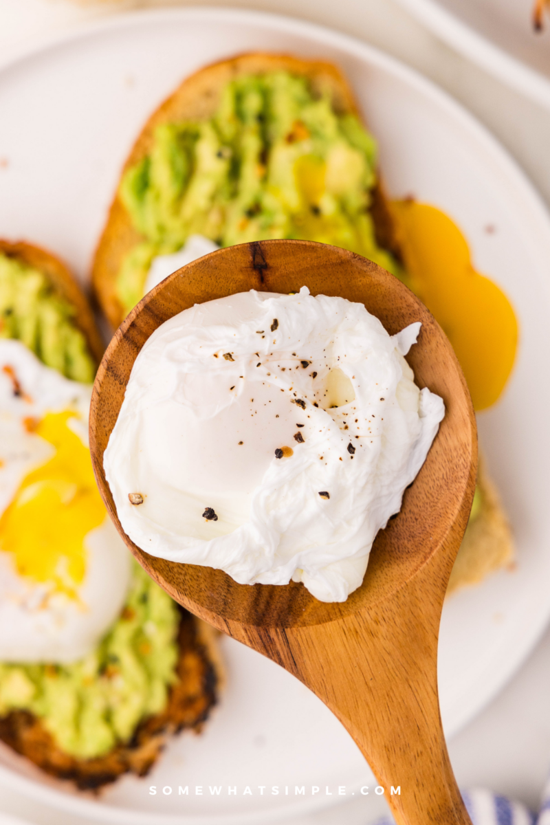 wood spoon holding a Poached Egg with avocado toast in the background
