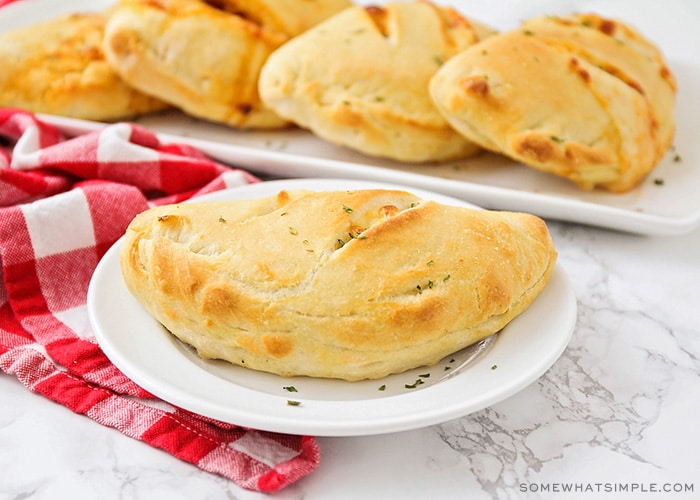 a freshly backed pizza pocket on a white plate with more on a serving tray behind it.