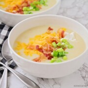 a bowl of baked potato soup topped with shredded cheese, bacon, green onion and sour cream
