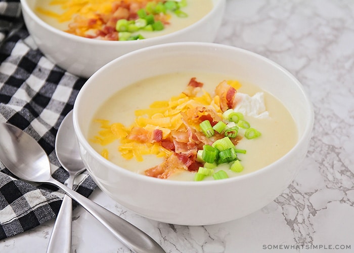 a bowl of baked potato soup topped with shredded cheese, bacon, green onion and sour cream