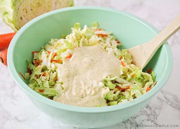 mixing coleslaw dressing in a bowl with shredded cabbage and carrots