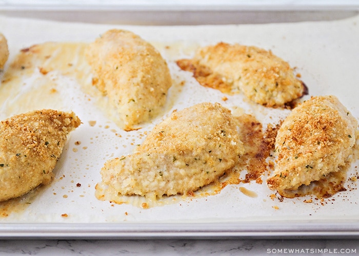 a baking sheet lined with parchment paper with five fully baked parmesan chicken breasts