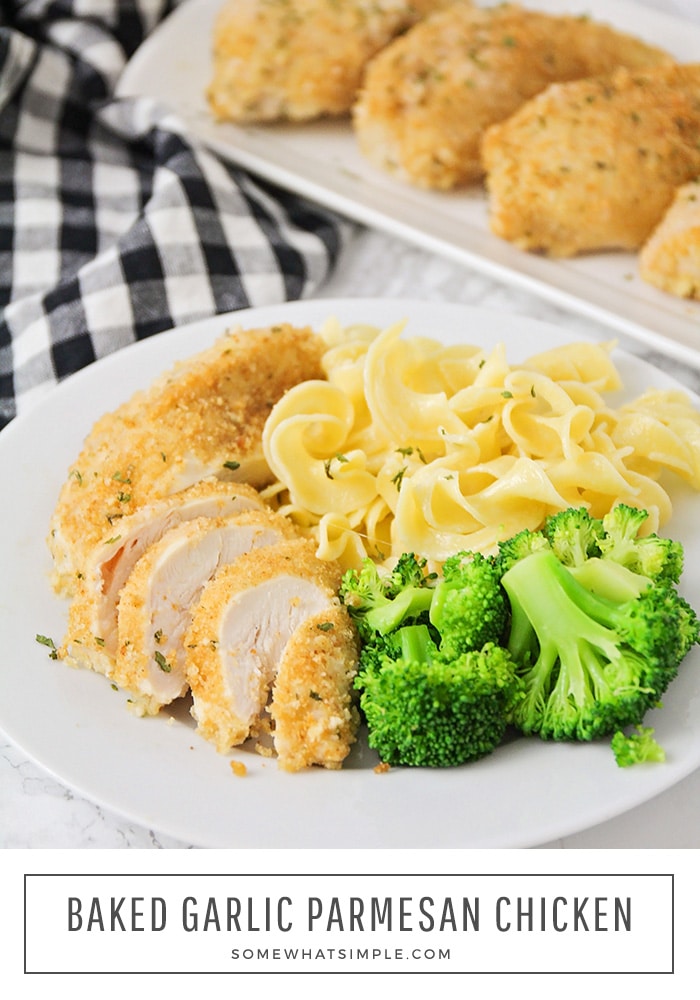 looking down on a white plate with a sliced breast of baked garlic parmesan chicken with a side of broccoli and pasta with a serving tray of more parmesan chicken in the background. A black and white checkered napkin is under the serving tray and plate. The words baked garlic parmesan chicken is written at the bottom of the image in a white box.