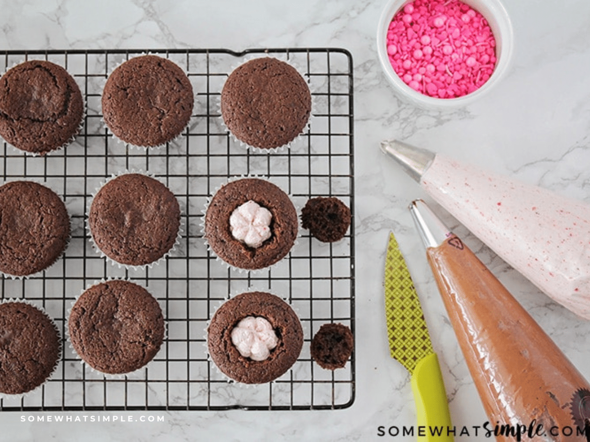 Chocolate fudge cupcakes on a cooling rack next to piping bags