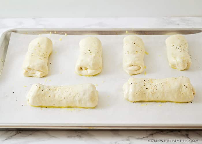 six ham and cheese rolls on a parchment lined baking sheet waiting to go in the oven.
