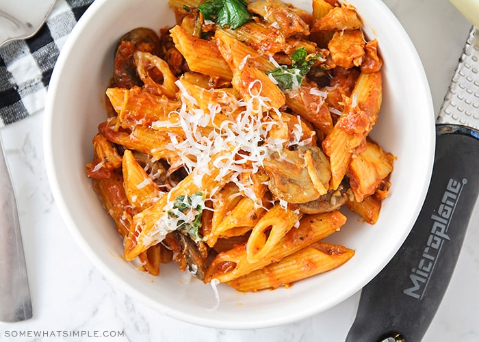 looking down on a bowl filled with chicken, pasta, mushrooms and topped with parmesan cheese