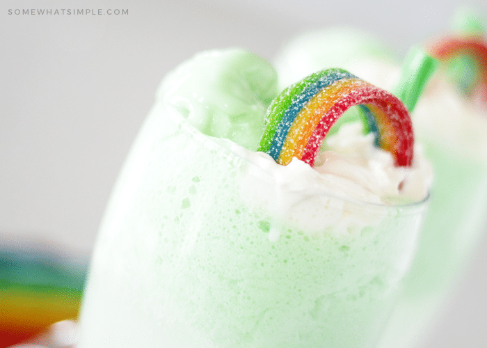 a green st. patricks day float topped with whipped cream and a rainbow piece of candy folded over to look like a rainbow.
