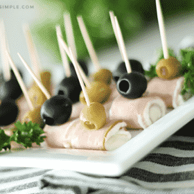 ham and cream cheese roll ups topped with black and green olives on a white serving tray