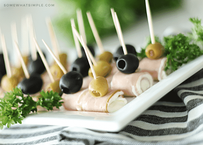 ham and cream cheese roll ups topped with black and green olives on a white serving tray