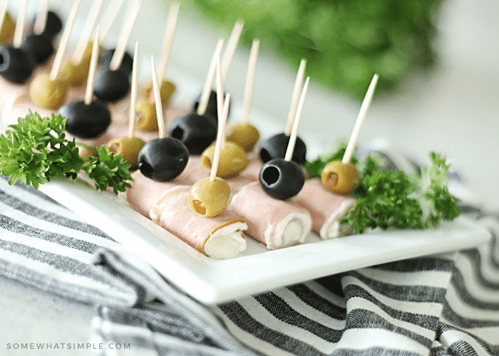 close up of cream cheese ham roll ups with green and black olives on a white plate