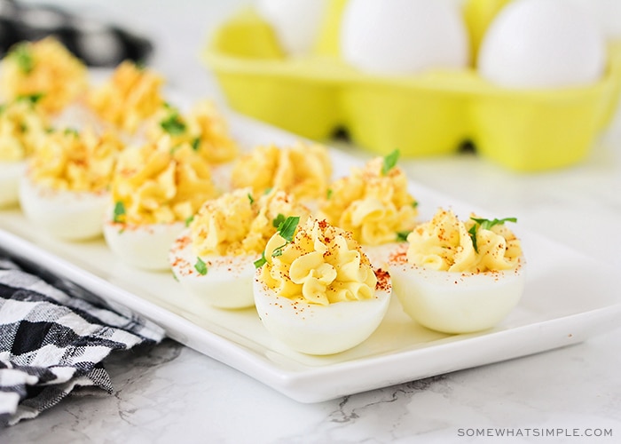 a long white serving tray filled with classic deviled eggs topped with paprika and parsley