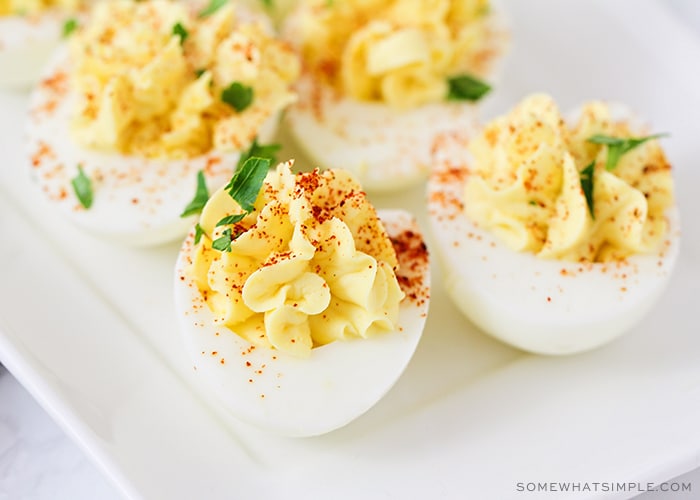 a close up of a deviled egg on a white serving tray that was made with this easy recipe. The egg is topped with a dash of paprika and shredded parsley.