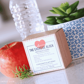 an exercise block with a funny printable on the outside sitting on a counter next to a bottle of water and an apple