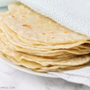 a stack of homemade flour tortillas wrapped in a blue and white towel on a white plate