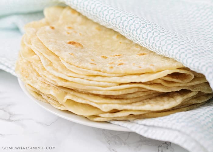 a stack of homemade flour tortillas wrapped in a blue and white towel on a white plate