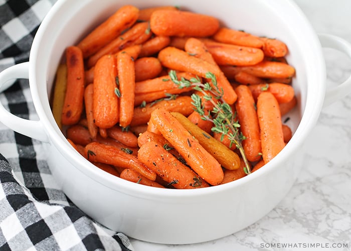 a white serving bowl that is filled with honey glazed carrots that have been baked and topped with thyme. A black and white checkered napkin is laying next to the bowl on the counter.