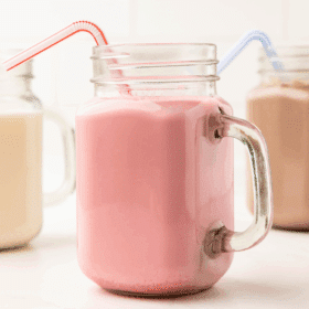 close up of 3 glasses filled with flavored milk and plastic straws