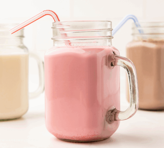 close up of 3 glasses filled with flavored milk and plastic straws