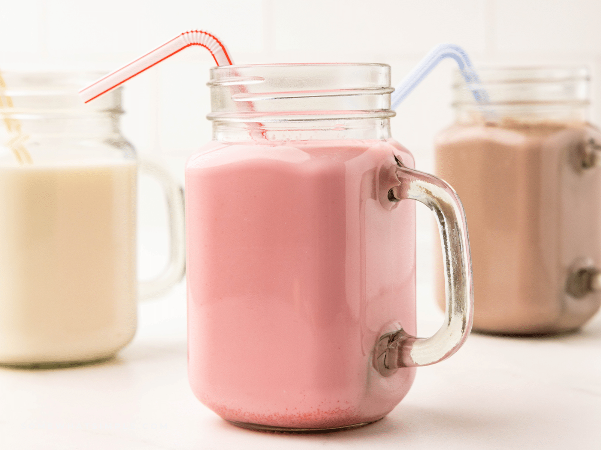 close up of 3 glasses filled with flavored milk and plastic straws