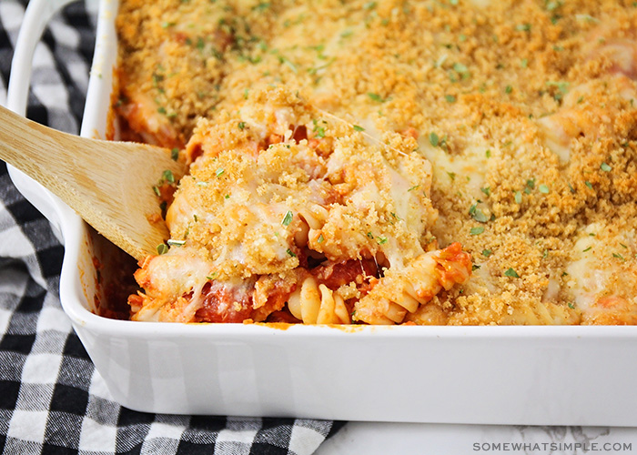 a close up of the chicken casserole with a wood spoon beginning to scoop out a serving. Melted cheese is beginning to stretch and the pasta underneath is revealed.