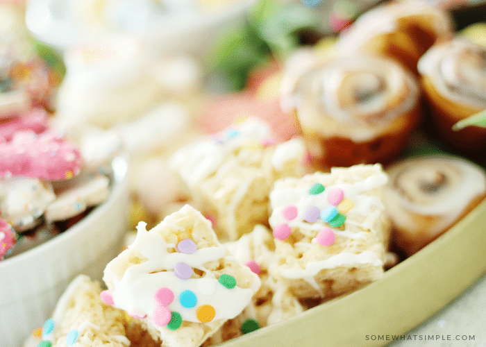 a close up of squared sugar cookie bars with pastel sprinkle dots with other cookies in the cookie tray in the background.