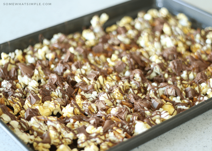 a baking sheet of gourmet popcorn mixed with small pieces of kit kat bars and pretzels with drizzled chocolate over the top