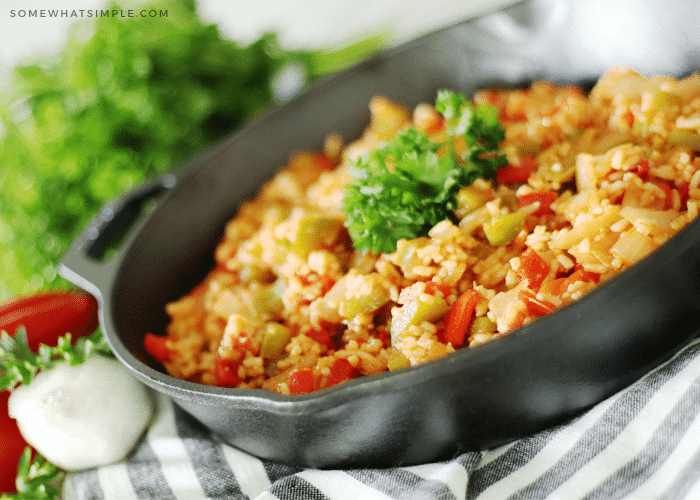 a cast iron skillet filled with homemade Spanish rice. Mixed in with the rice are slices of red and green bell peppers and a small pinch of parsley is in the center of the rice.
