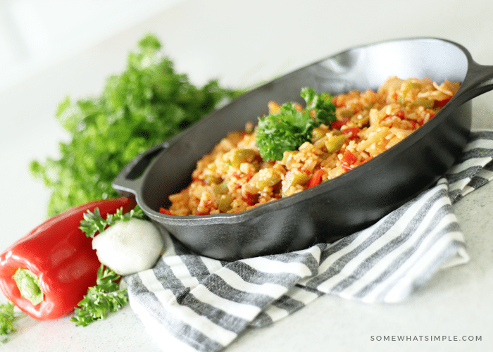 a black iron skillet sitting on a counter filled with this easy homemade Mexican rice recipe. Next to the skillet is a red bell pepper and onion and a bundle of parsley.