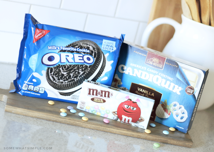 a package of oreos, a box of m&ms and a box of baking chocolate on a counter which are the ingredients to make chocolate covered oreos.