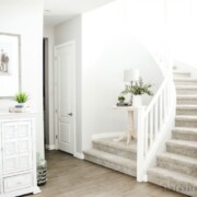 the entry way of a home with a winding staircase. A small wooden table is on an elevated landing. There is also a large white cabinet along the wall in the entry way.