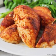 a white plate filled with baked bbq chicken breasts with leaves of green salad next to it on the plate.