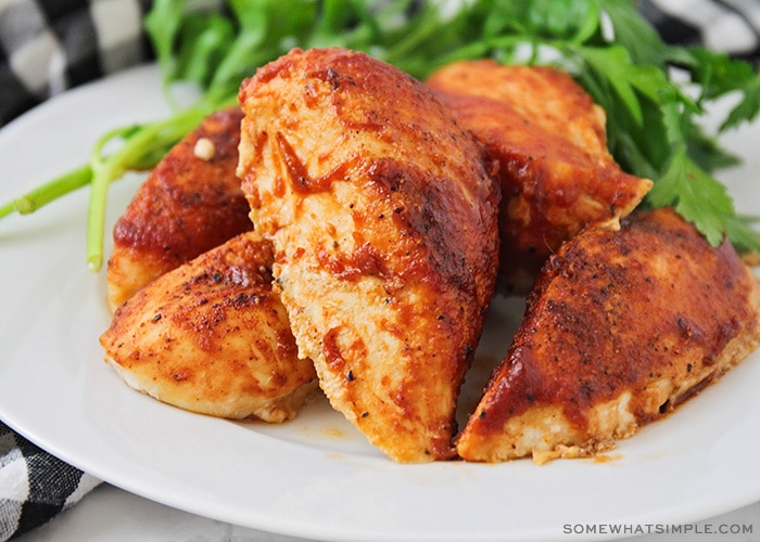 a white plate filled with baked bbq chicken breasts with leaves of green salad next to it on the plate.