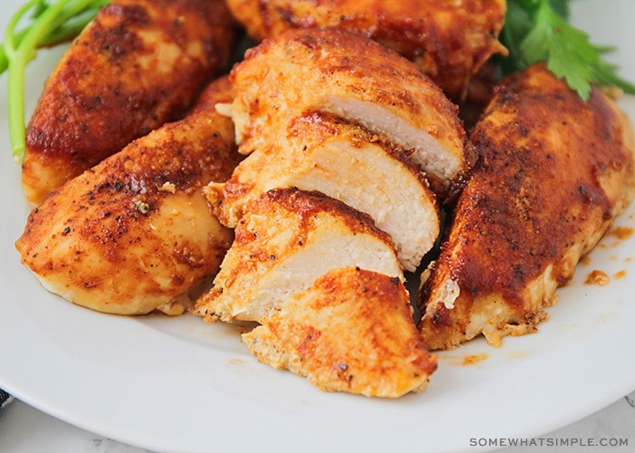 a close up of a plate of oven baked bbq chicken breasts on a white plate. One of the breasts has been sliced into bite-sized pieces.