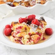 a white plate filled with baked raspberry french toast that is topped with fresh whole raspberries and syrup