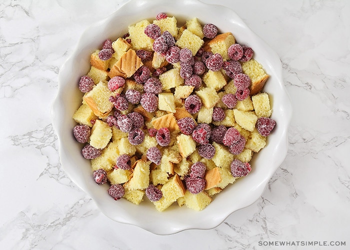 looking down on a white bowl filled with bread cubes and frozen raspberries