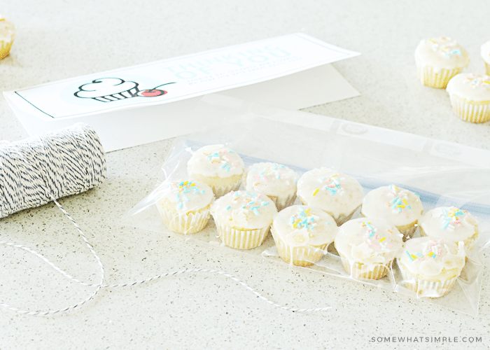 a gift tag printable, baker's twine and a bag with mini cupcakes inside sitting on a counter