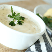 a small white bowl filled with a homemade Alfredo sauce topped with a small piece of parsley for garnishment