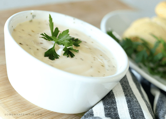 a small white bowl filled with a homemade Alfredo sauce topped with a small piece of parsley for garnishment 